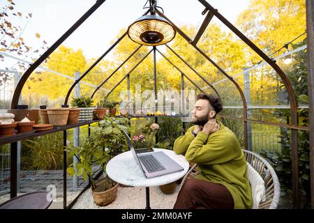 Man works remotely on laptop in glasshouse at backyard Stock Photo