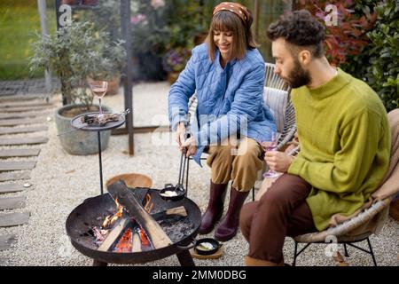 Young couple spending dinner time by the fire at backyard Stock Photo