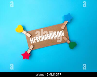 Wooden clips and brown card with the word MERCHANDISING on blue background. Stock Photo