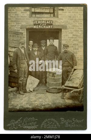 Original Victorian cabinet card of group of fishermen / traders / porters outside the fish merchants of J.E. Borlace, with catch of fish, including a skate held up by one man, and a hand cart with wrapped produce, barrels advertising merchant's name, at the quayside, Brixham, Devon, U.K.  By photographer Peth K. Kitto (maybe Frederick K ) circa 1890's.