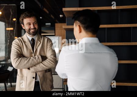 Adult multiracial businessmen smiling and talking while standing in office lobby Stock Photo