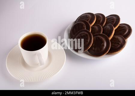 photo one coffee cup with coffee stands next to a full plate of chocolate-covered cookies on a white background view from above Stock Photo