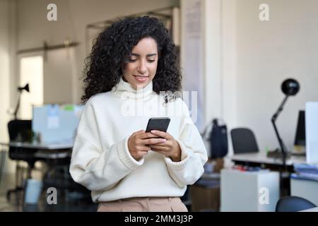 Smiling young business woman manager using phone standing in office. Stock Photo