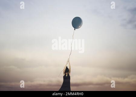 woman clings to a balloon flying in the sky, abstract concept Stock Photo
