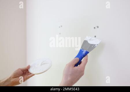 Builder or repairman with putty knife plastering white wall close up. Stock Photo