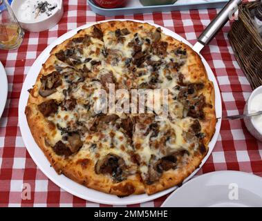 Delicious pizza with lamb serving on a table with plaid tablecloth in a tavern. Stock Photo