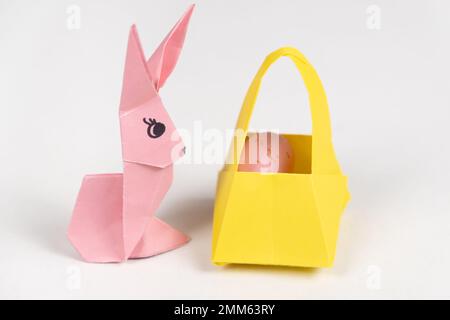 An Easter bunny figurine made of paper, origami, and a basket with eggs on a white background Stock Photo