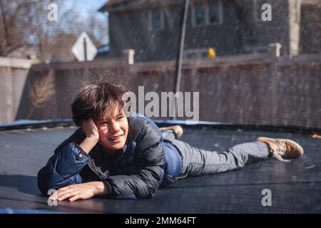 A smiling boy lays on a trampoline outside in winter Stock Photo