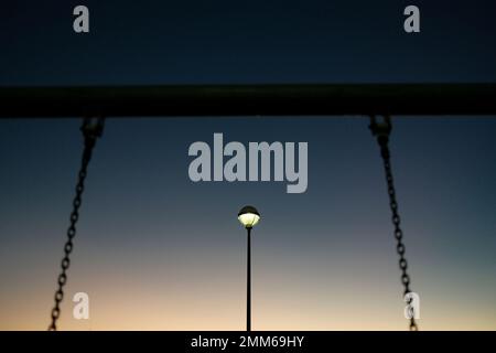 Swing chain against glowing light in playground Stock Photo