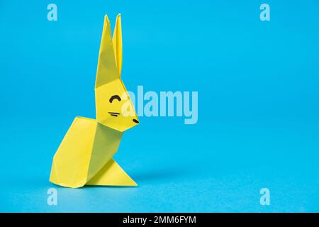 A yellow origami rabbit on a blue background. Crafts for Easter, fold from paper, do it yourself, place for text Stock Photo