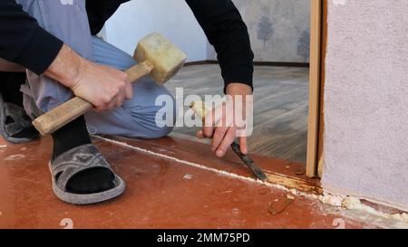 carpenter works with a mallet and a chisel in a home room leveling a wooden threshold in a doorway, leveling the plane of an interior door threshold Stock Photo