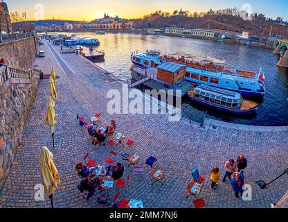 PRAGUE, CZECHIA - MARCH 11, 2022: The outdoor restaurant on the riverfront with great view on evening city skyline, on March 11 in Prague, Czechia Stock Photo