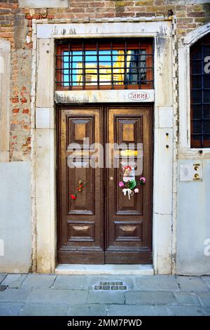 On Holocaust Remembrance Day 2023, an anonymous hand pinned the picture of three children and some flowers on the old door at number 5999 Cannaregio, in Venice. The children were deported to Auschwitz, with their parents and one-year-old brother, in 1943. They were 14, 10, 7 years old. They were killed in Auschwitz on February 26, 1944 with their one-year-old brother. Some years ago, 7 'stumbling stones' were put at the entrance of their house. A note under the photo says: ' Anna, Guido, and Giorgia Dina. Leone was one year old, and we will never know what face he had'. Stock Photo