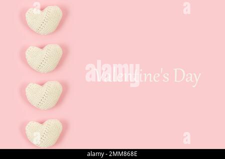 Many white knitted hearts with an inscription "Valentine's day" on pink background. Concept of Valentine day. Greeting card for Valentine. Greeting ca Stock Photo