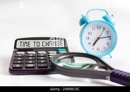 TIME TO CHANGE text on calculator display, blurred focus of clock and magnifier on white background Stock Photo