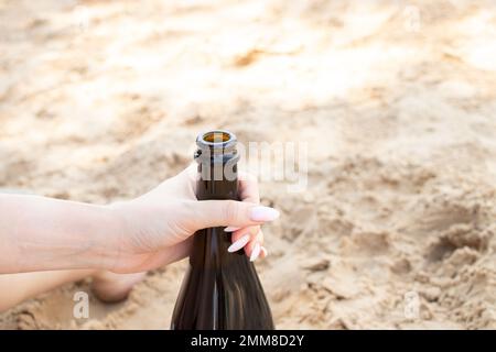 a female hand holds a bottle of sparkling wine on the beach in summer on vacation, a bottle of champagne Stock Photo
