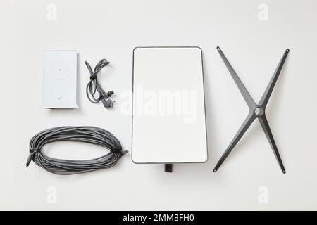 KYIV, UKRAINE - JANUARY 24, 2023: Basic Starlink kit, antenna, wi-fi router, base and cables, top view on white background. Stock Photo