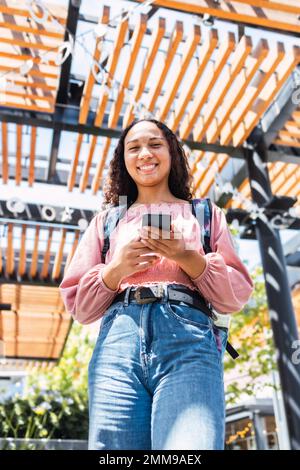 Latin university student woman smiling and using her smart phone. Looking at camera Stock Photo