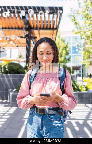 Latin university student woman smiling and using her smart phone outside the mall in her free time Stock Photo