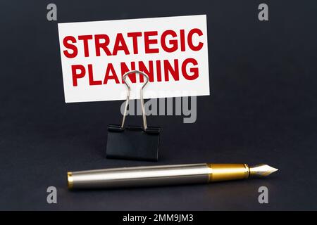 Business concept. On the black surface is a pen, an office paper clip with a business card on which is written - STRATEGIC PLANNING Stock Photo