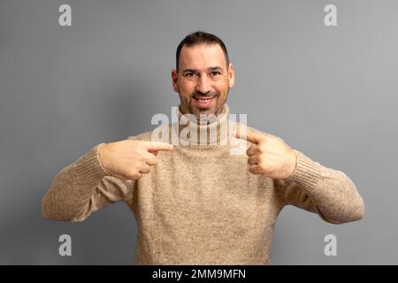 Handsome bearded hispanic man wearing turtleneck looking confident with smile on his face, pointing fingers to himself proud and happy Stock Photo