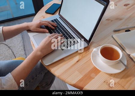 Woman using laptop with white screen. Mobile phone, laptop and cup of tea on the wooden table. Stock Photo