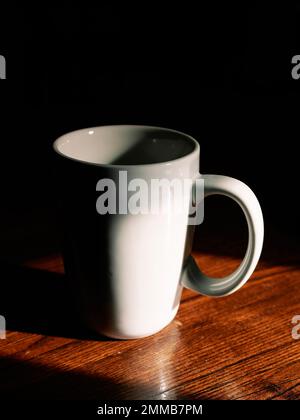 Empty white ceramic coffee cup in shadow on a restaurant table. Stock Photo