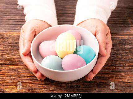 Stylish easter dyed colorful eggs on white plate, wooden rustic background, woman hands Stock Photo