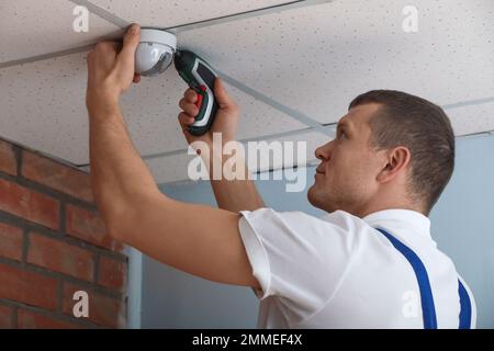 Technician installing CCTV camera on ceiling indoors Stock Photo