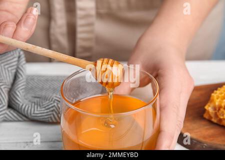 Woman with honey and dipper at white wooden table, closeup Stock Photo