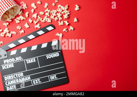 Clapper board and popcorn on red background, flat lay with space for text. Visiting cinema Stock Photo