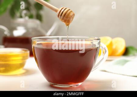 Honey dripping into cup of tea on white table Stock Photo