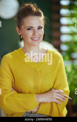 Portrait of happy modern small business owner woman in yellow sweater standing in the modern green office. Stock Photo