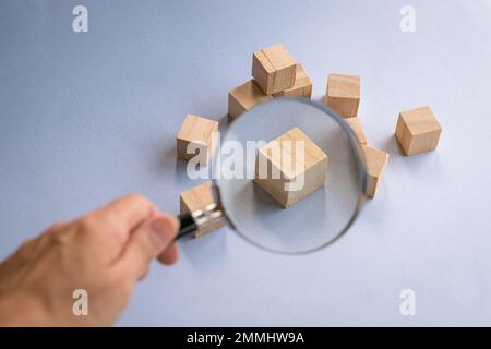 Hand holding a magnifying glass over wooden block. Head hunt, recruitment or leadership concept. Stock Photo
