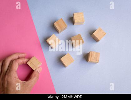 Wooden blocks on blue and pink background with a hand picking one of the blocks. Leadership, human resources, team or hiring concept. Stock Photo