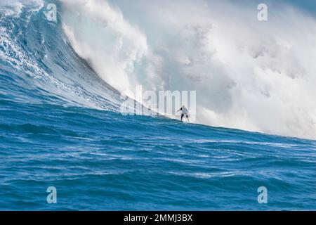 A tow-in surfer (MR) drops to the curl of Hawaii's big surf at Peahi (Jaws) off Maui, Hawaii, USA. Stock Photo