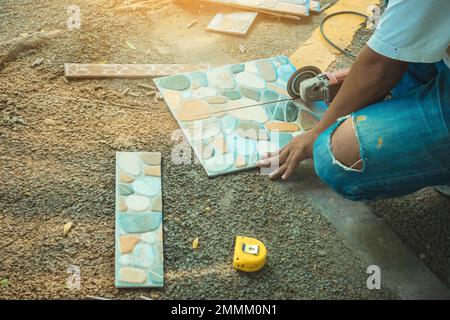 Hands of construction worker using an angle grinder for cutting the tiles at construction site. Man worker cutting beige tile with a circular saw. Cut Stock Photo