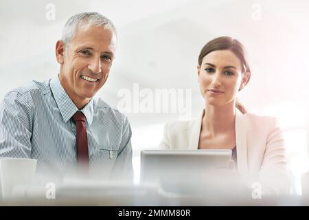 We grabbed success and ran with it. Portrait of two coworkers sitting at a table using a digital tablet. Stock Photo