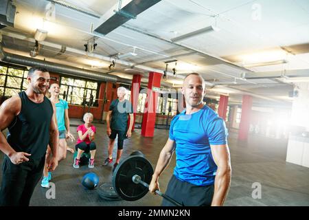 Winners train, losers complain. a young man lifting weights while a group of people in the background watch on. Stock Photo