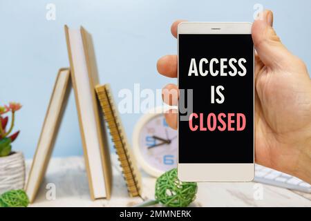 Smartphone in hand with the inscription ACCESS IS CLOSED next to office supplies Stock Photo