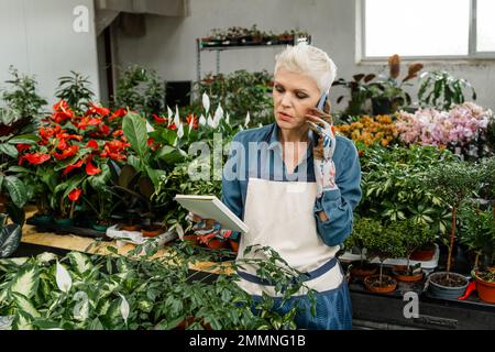 Woman working at plant nursery. Smiling woman gardener writing orders Stock Photo