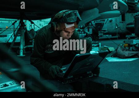 U.S. Marine Corps Sgt. Joaquin Aldape, an F-35B power line mechanic with Marine Medium Tiltrotor Squadron 262 (Rein.), 31st Marine Expeditionary Unit, uses a computer during maintenance of an F-35B Lightning II jet aboard Amphibious Assault Ship USS Tripoli (LHA 7), in the Philippine Sea, Sept. 21, 2022. F-35B maintainers, supported by Sailors operating a crane for lifting, regularly perform maintenance to ensure the aircraft’s readiness for flight operations. Aldape is a native of Decatur, Texas. The 31st MEU is operating aboard ships of the Tripoli Amphibious Ready Group in the 7th Fleet are Stock Photo