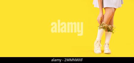 Legs of beautiful young woman with flowers in socks on yellow background with space for text Stock Photo