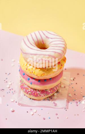 Parchment with different delicious donuts on pink table near yellow wall Stock Photo