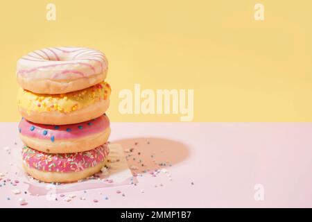 Parchment with different delicious donuts on pink table near yellow wall Stock Photo