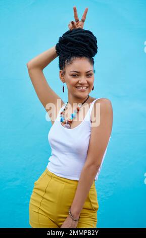 Charming personality and style to match. Portrait of a trendy young woman making a bunny ears gesture against a blue background. Stock Photo