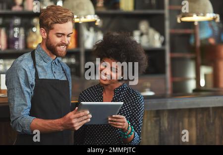 Reading the comments on their cafes website. young coffee shop workers using a digital tablet together. Stock Photo