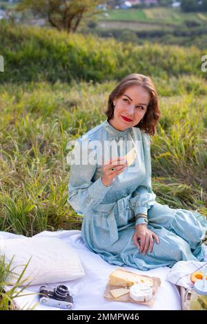 A woman in blue dress sits on a picnic in a park with panoramic view Stock Photo
