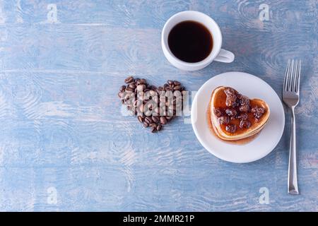 Breakfast for dad. Homemade heart shaped pancakes with berry jam, heart shape made from coffee beans, white cup of coffee and fork on blue wooden tabl Stock Photo