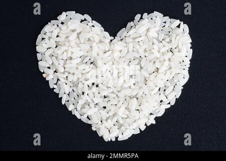 Diet food concept. Love for rice. Heart shaped uncooked rice isolated on black background, closeup, top view. Can be used as a symbol of Thai, Japanes Stock Photo